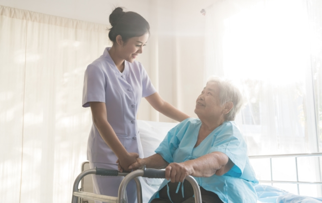 Nurse supporting elderly woman in using walker